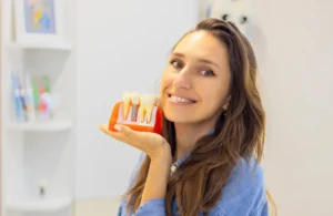 A woman smiles while holding a dental implants display next to her chin.