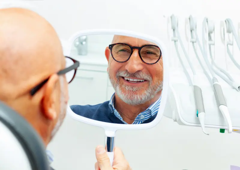 A happy patient looks at their smile in a mirror after a dental implant procedure.